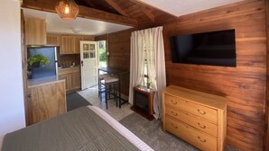 A compact room with a bed, a wooden dresser, a TV, and a kitchenette. - Cozy Cottage near Bigfork overlooking Flathead Lake in our Cherry Orchard (Bigfork)