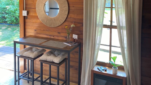 A wooden interior with a table, chairs, a mirror, a hanging light fixture, and a window with curtains. - Cozy Cottage near Bigfork overlooking Flathead Lake in our Cherry Orchard (Bigfork)