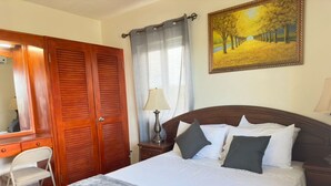 Una camera da letto arredata con un letto, una scrivania, una sedia, un armadio, una lampada e un quadro appeso al muro.