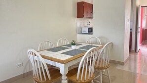Zona pranzo con tavolo rettangolare, sei sedie bianche e cucina visibile attraverso un'apertura.
