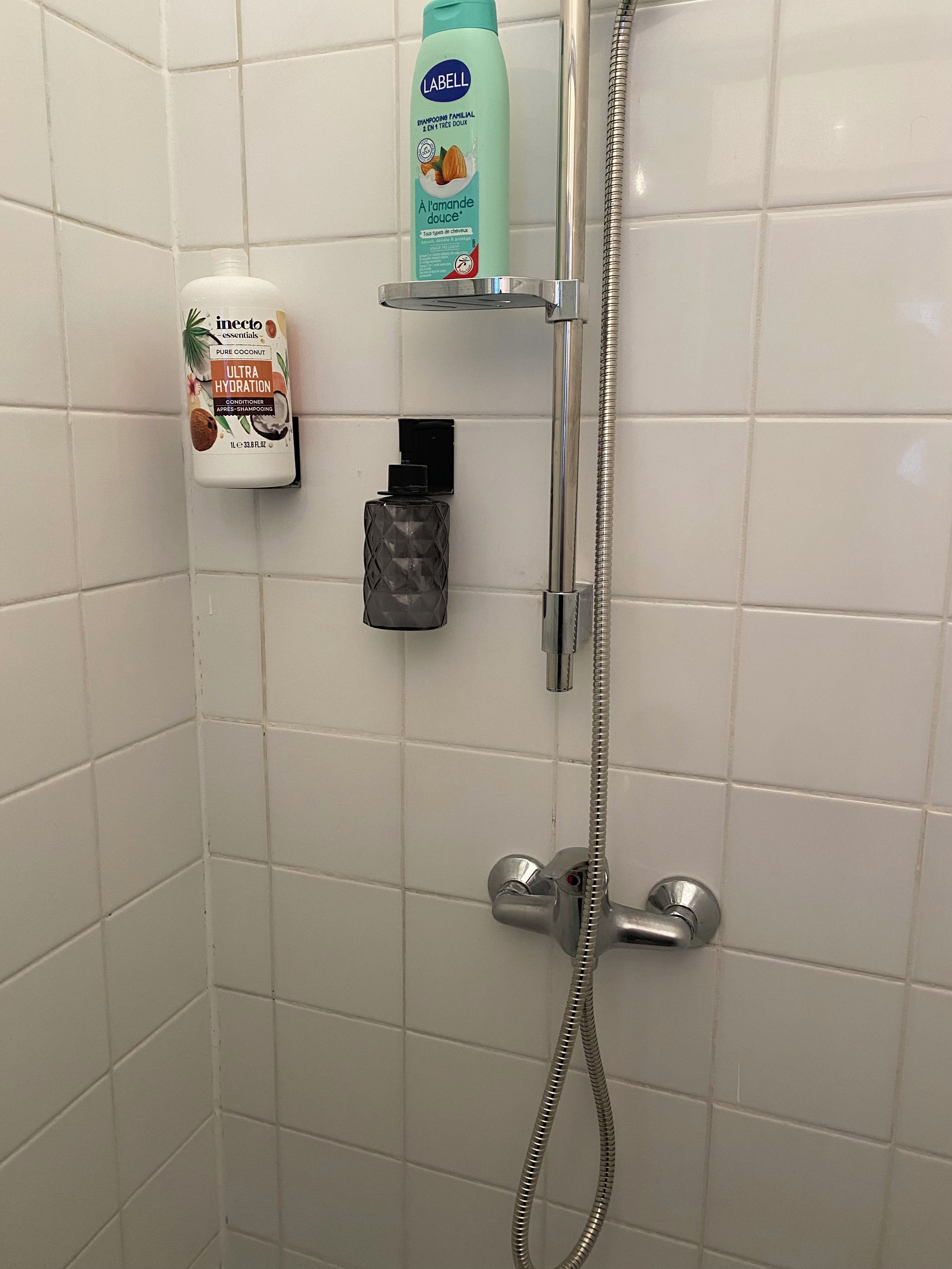 Een douchegedeelte met een handdouche, een fles shampoo en een fles conditioner.
