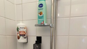 A shower area with a handheld showerhead, a bottle of shampoo, and a bottle of conditioner.