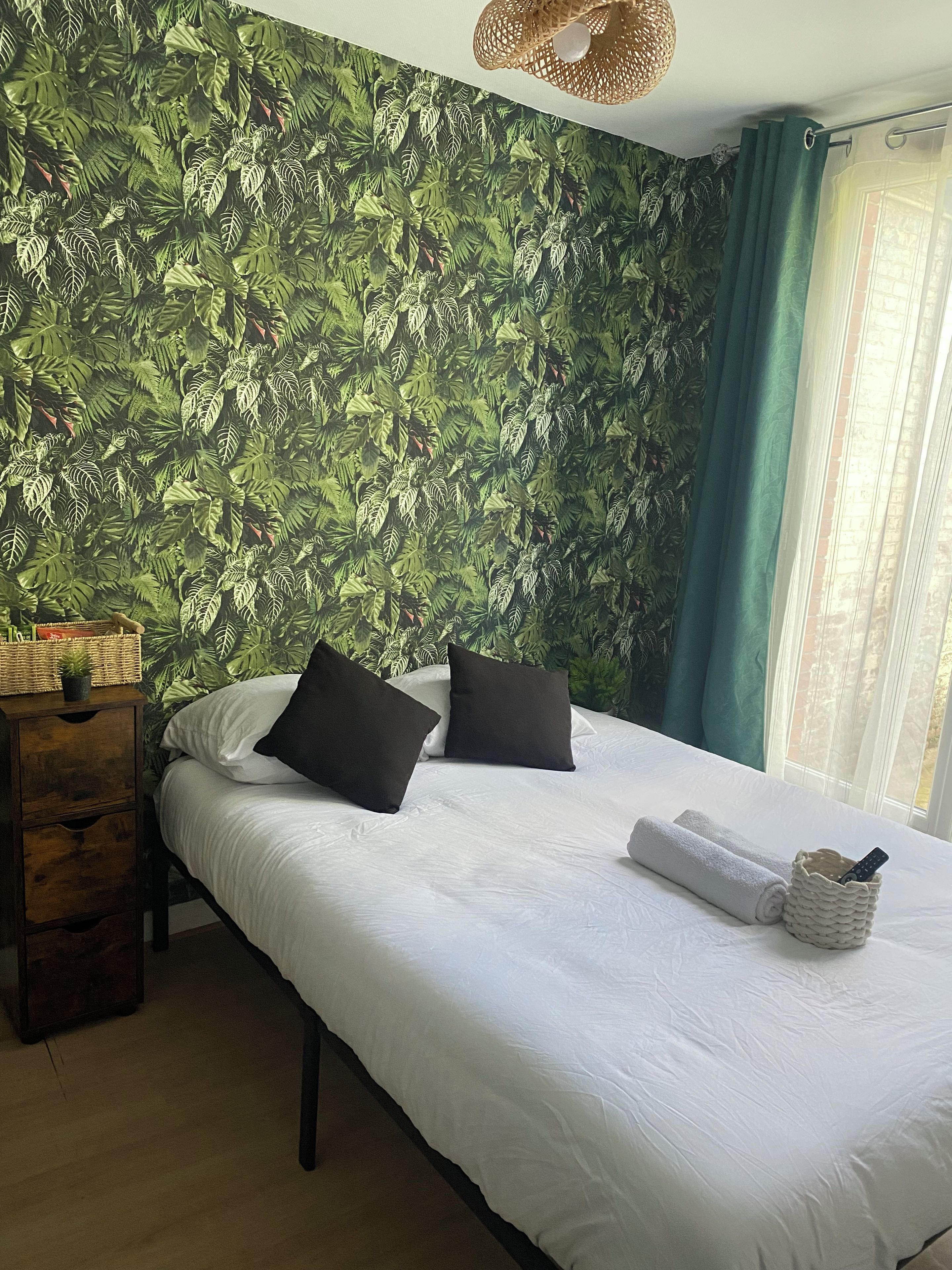 Een hotelkamer met een bed, kussens, een nachtkastje met lamp en een raam met gordijnen.