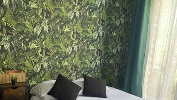 Een hotelkamer met een bed, kussens, een nachtkastje met lamp en een raam met gordijnen.