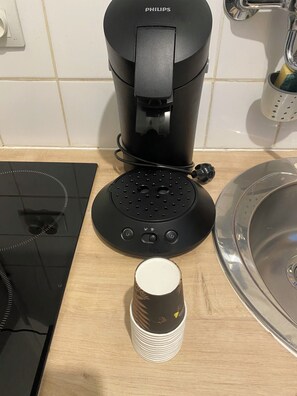 En kaffebryggare, en kopp och ett handfat på en köksbänk.