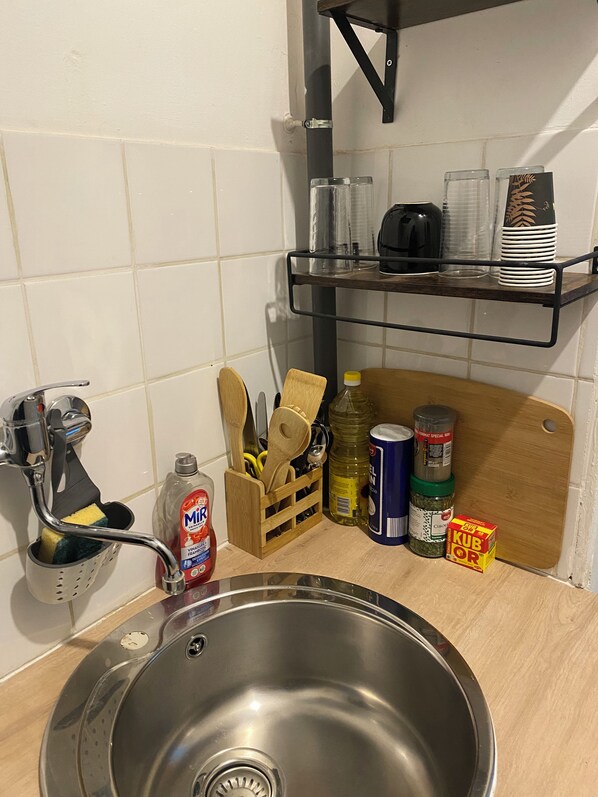 A kitchen with a stainless steel sink, a wooden cutting board, and various kitchen utensils and appliances.