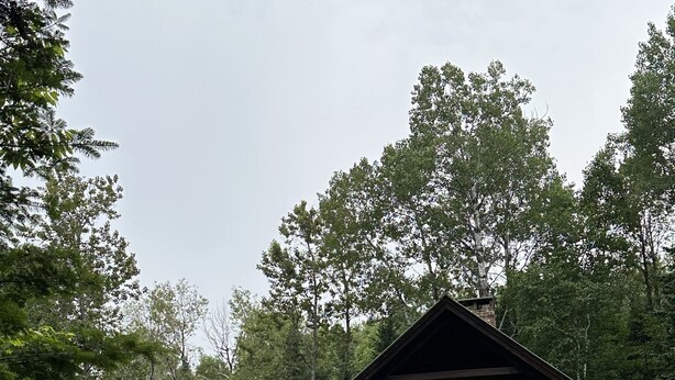 A log cabin with a porch, a red umbrella, and a bench.