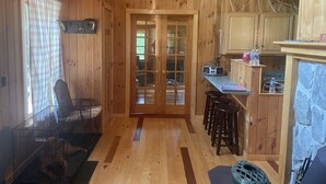 A wooden interior with a kitchen area, a dining table with stools, and a pet enclosure.