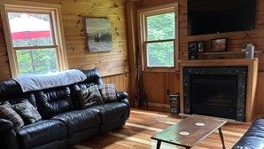 A cozy cabin interior with a leather sofa, a wooden coffee table, and a fireplace.