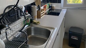 Una cocina con armarios blancos, un lavamanos de acero inoxidable y una ventana con vistas a edificios.