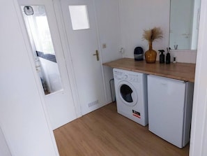 A compact laundry room with a washing machine and dryer, a wooden countertop, and a mirror.