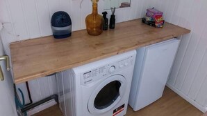 Un área de lavandería compacta con lavadora, secadora, encimera de madera, un florero con plantas secas y un espejo.