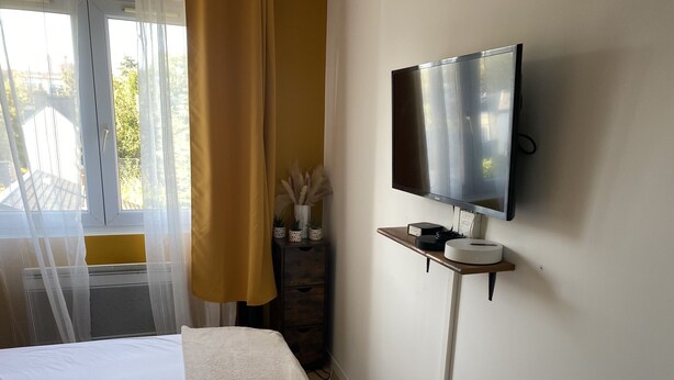 Una habitación de hotel con una cama, un televisor montado en la pared y una mesita con un control remoto.
