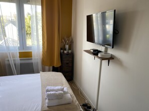 A hotel room with a bed, a TV mounted on the wall, and a small table with a remote control. - The Sympathetic One (Rouen)