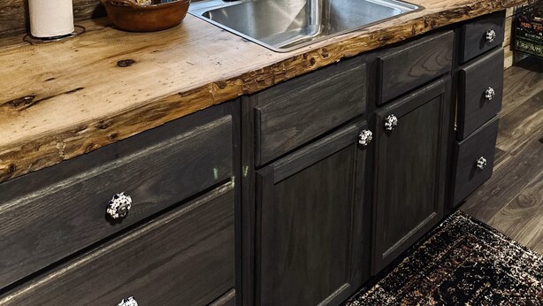 Una cocina rústica con interior de madera, un ventanal grande y un lavamanos de acero inoxidable.