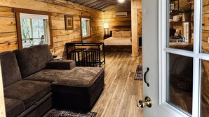 Interior acogedor de una cabaña con paredes de madera, un sofá, una cama y un comedor.