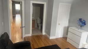 Uma sala de estar moderna com piso de madeira, um sofá de couro preto, um aparador branco e um tapete preto.