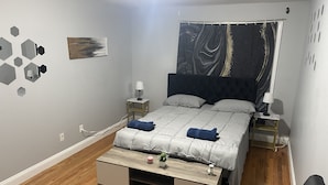Quarto moderno com cama, mesas de cabeceira, escrivaninha e uma cadeira.
