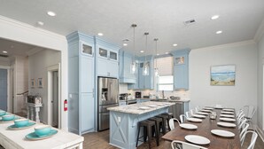 Una cucina moderna con mobili blu, una grande isola e sedie bianche attorno a un tavolo da pranzo in legno.