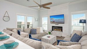 Un soggiorno moderno con camino, ventilatore a soffitto e una grande TV.