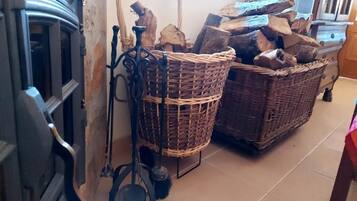 Takka, jossa on metallinen arina, kaksi rottinkikoria täynnä puita ja metallinen lapio.