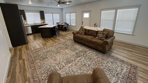 A spacious living area with a brown sofa, patterned rug, and a kitchen area with a bar and dining table. - Beautiful Modern Lake House Along Lake Oahe. (Pierre)