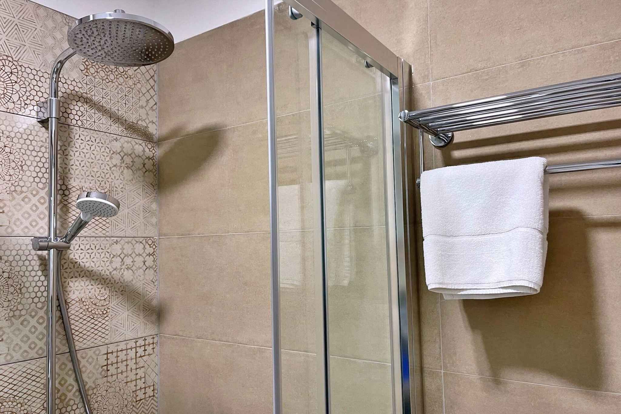 Een douche met een glazen deur, een handdoekrek met een handdoek en een betegelde muur.