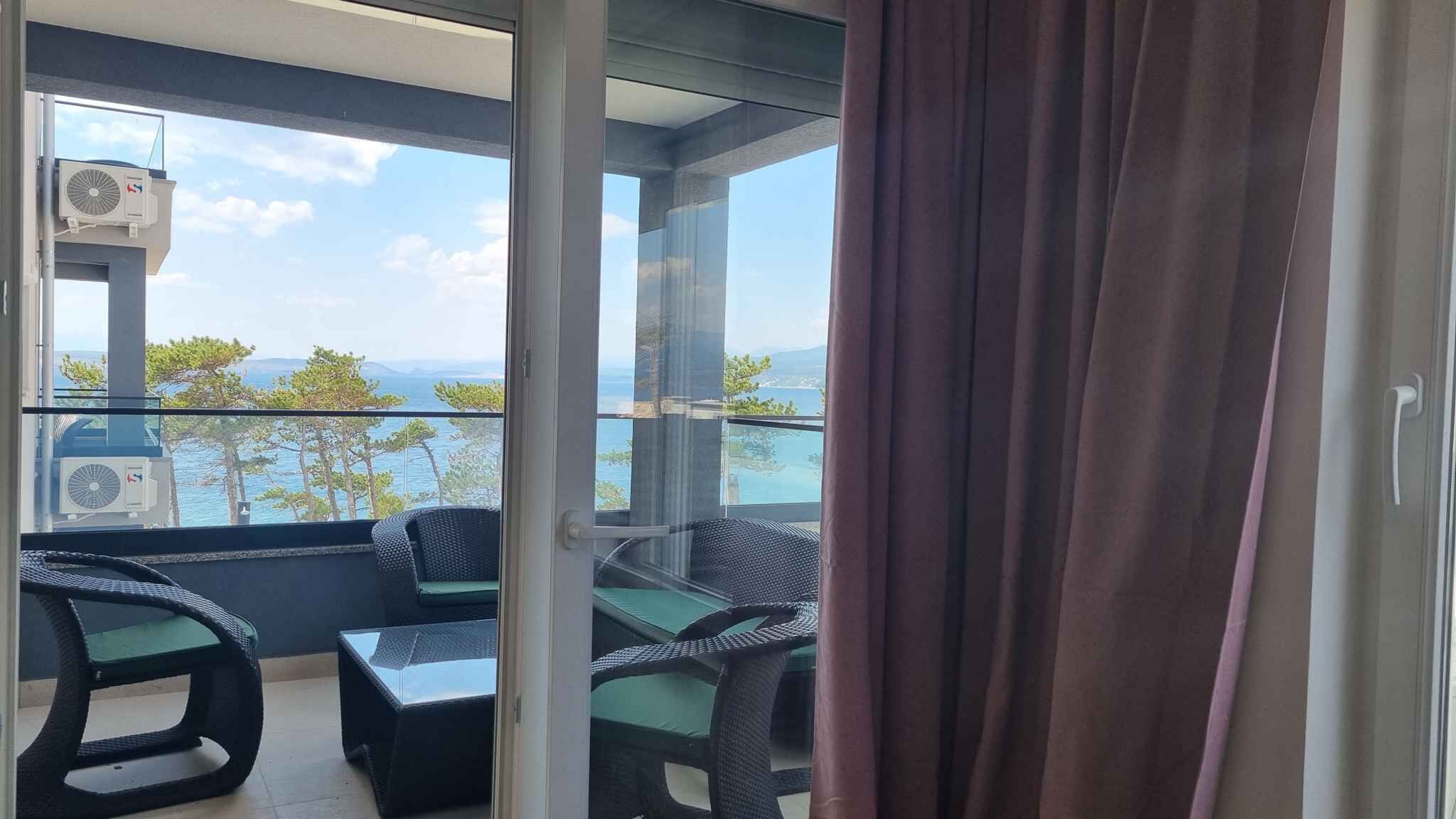 A balcony with wicker furniture, a glass door, and a view of the sea and mountains.