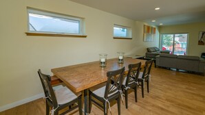 A dining area with a wooden table and chairs, two windows, a sofa, and a view of the outside. - Modern Times (Big Bear Lake)