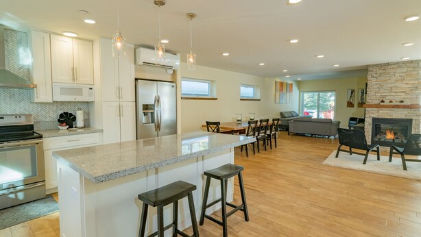 A modern kitchen with a central island, bar stools, and a dining area with a fireplace. - Modern Times (Big Bear Lake)
