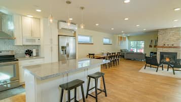 A modern kitchen with a central island, bar stools, and a dining area with a fireplace.