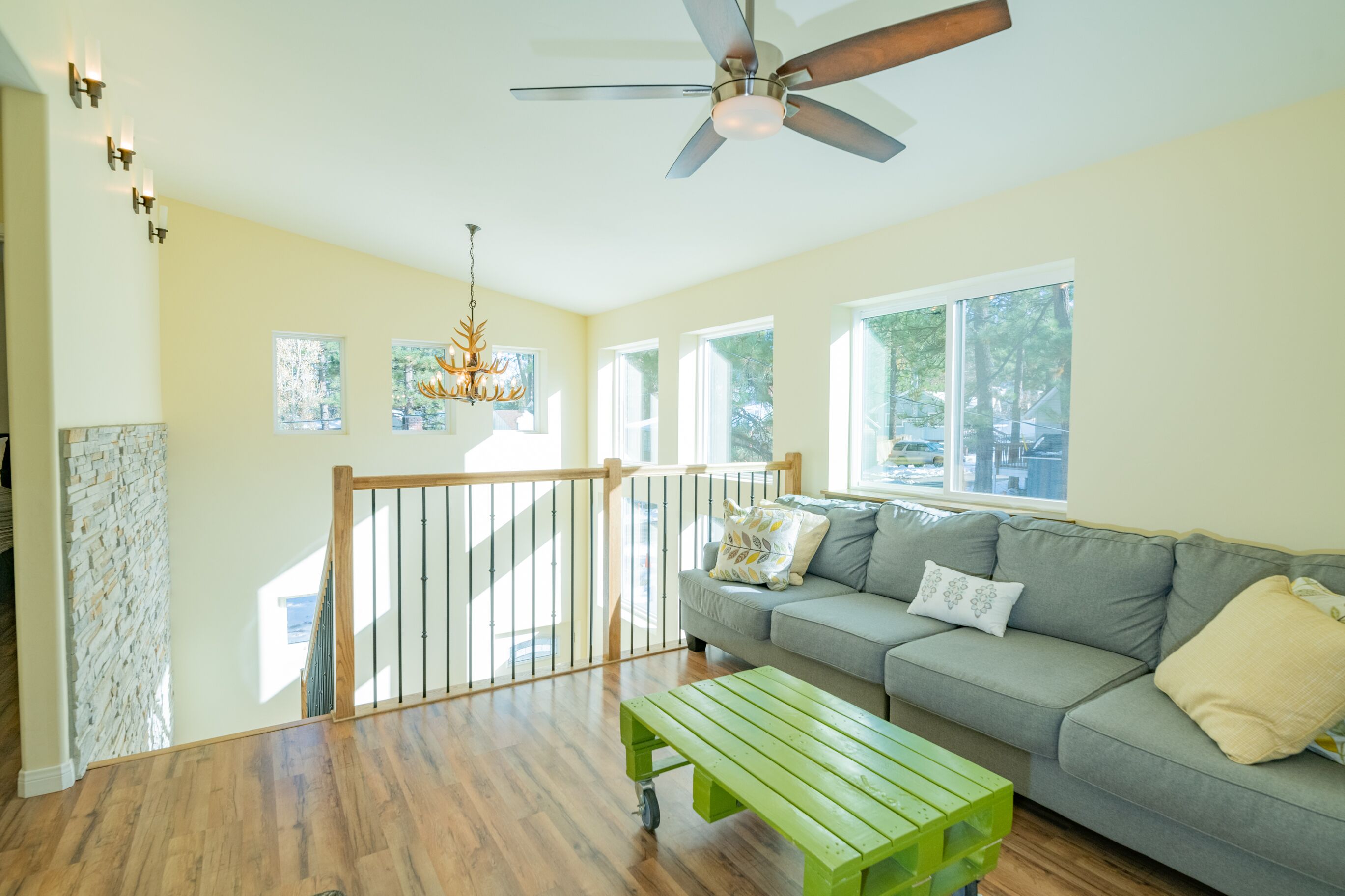 A spacious living room with a wooden floor, a grey sofa, a green coffee table, and a ceiling fan.