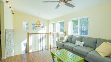 A spacious living room with a wooden floor, a grey sofa, a green coffee table, and a ceiling fan.