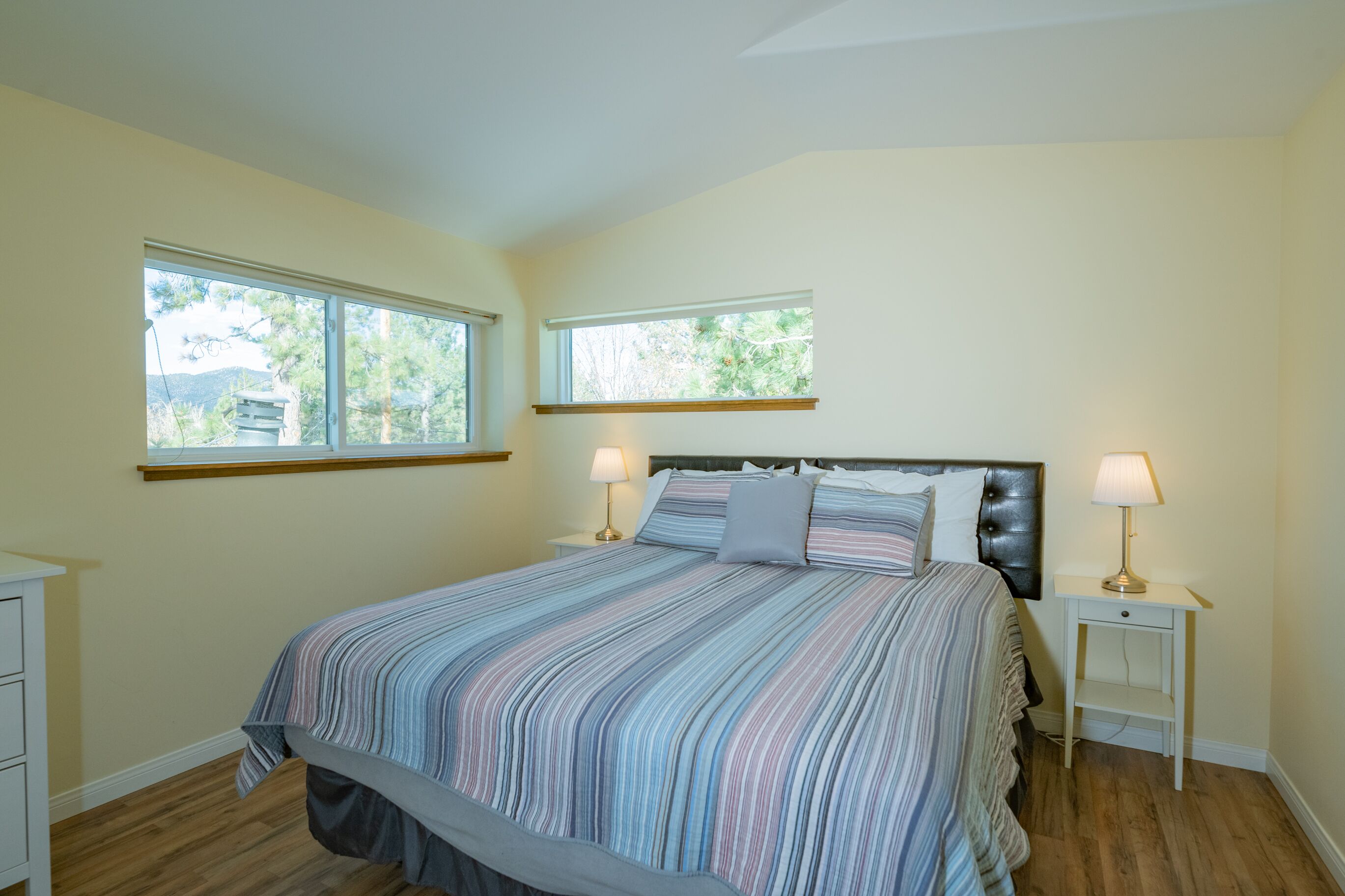 A bedroom with a large bed, two bedside tables, and two windows.