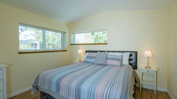 A bedroom with a large bed, two bedside tables, and two windows.