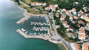 An aerial view of a coastal area with a marina, residential buildings, and a road.