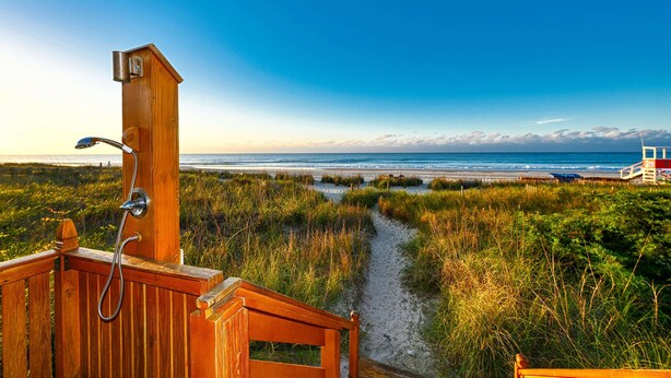 A wooden deck with a shower, a sandy path leading to the beach, and a lifeguard tower in the background. - Windy Hill Dunes-Oceanfront 3BD-Family Friendly (North Myrtle Beach)