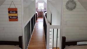 A narrow hallway with wooden floors and white walls, leading to a room with a window.