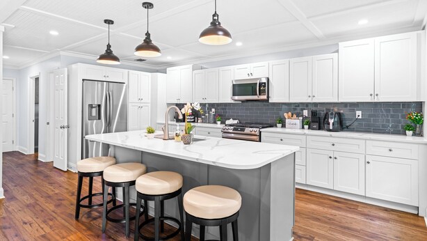 A modern kitchen with white cabinets, a stainless steel refrigerator, a microwave, and a large island with stools. - NEW IMMACULATE and quiet 4br Retreat between SAV DownTown & Tybee Island (Savannah)