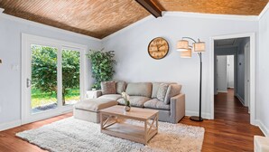 A living room with a wooden ceiling, a sofa, a coffee table, a clock, and a floor lamp. - NEW IMMACULATE and quiet 4br Retreat between SAV DownTown & Tybee Island (Savannah)