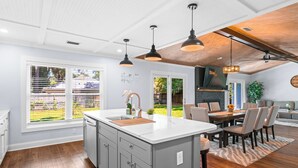 A modern kitchen with a large island, pendant lighting, and a dining area with chairs and a table. - NEW IMMACULATE and quiet 4br Retreat between SAV DownTown & Tybee Island (Savannah)