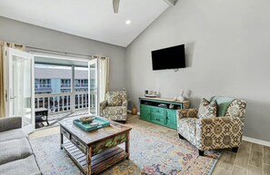Relax in this stylish living room with a sofa, coffee table, and flat-screen TV, plus a sliding door leading to a balcony with a city view.