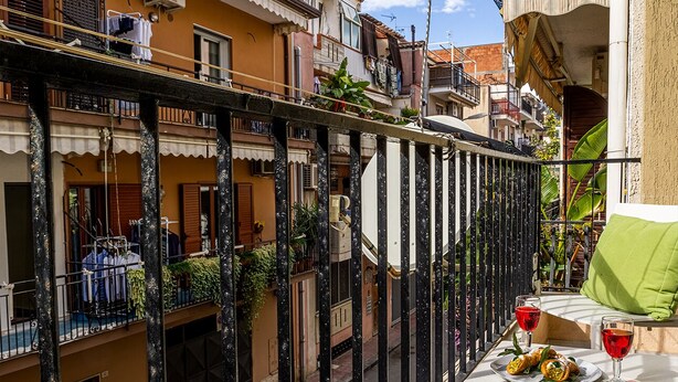 Un balcón con mesa lista para dos personas, que incluye un plato de comida y dos copas de vino tinto.