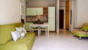 Un espacio habitable compacto con un sofá verde, una mesa de comedor con sillas y una zona de kitchenette.