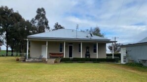 A single-story house with a front porch, a covered patio, and a well-maintained lawn. - Authentic Farm Cottage (Cowra)