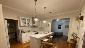 A compact kitchen with a central island, wooden chairs, and pendant lighting. - Authentic Farm Cottage (Cowra)