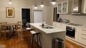A modern kitchen with a central island, bar stools, and pendant lighting. - Authentic Farm Cottage (Cowra)