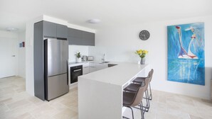 A modern kitchen with a central island, stainless steel appliances, and a painting on the wall. - Ocean Views at Sandrift on Nobby Beach (Gold Coast)