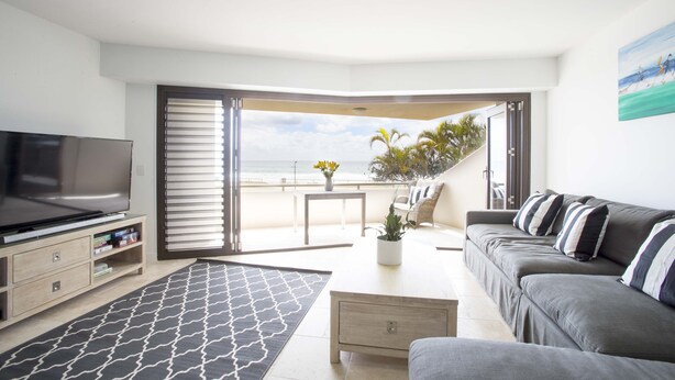A living room with a TV, sofa, coffee table, and a view of the beach. - Ocean Views at Sandrift on Nobby Beach (Gold Coast)