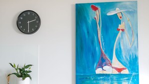 A dining area with a clock, chairs, a table, a potted plant, and a painting. - Ocean Views at Sandrift on Nobby Beach (Gold Coast)
